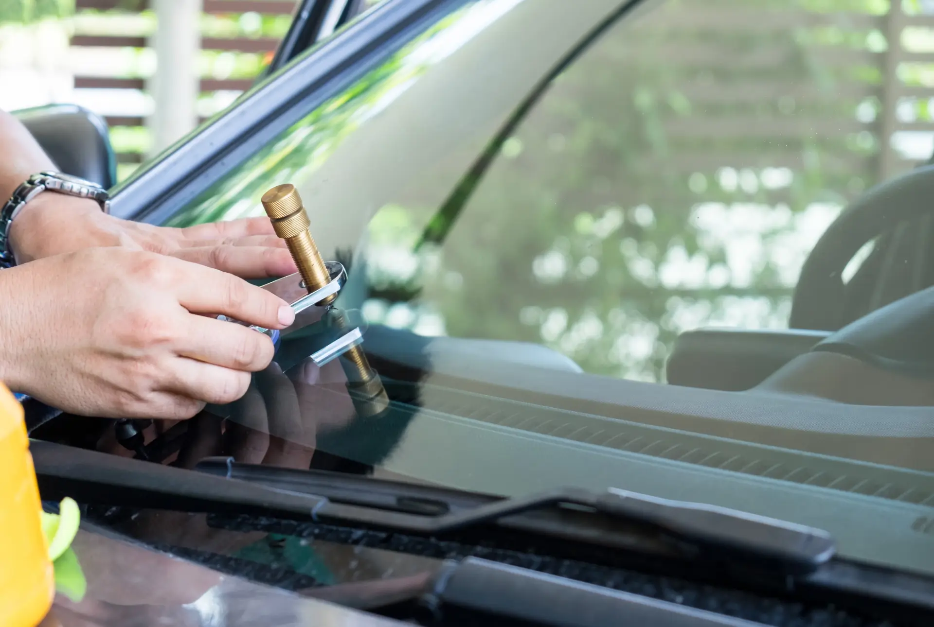 Hands using a brass chip repair tool on a windscreen outdoors